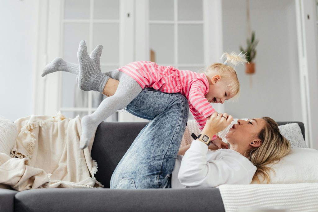mother lying on back on couch toddler balancing on legs